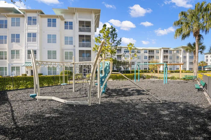 Modern apartment complex with a vibrant playground and lush greenery under a clear blue sky.