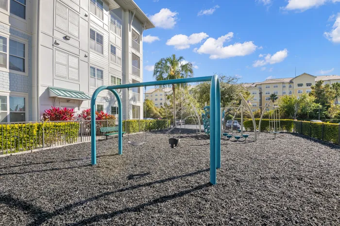Inviting apartment complex featuring a vibrant playground with swings and climbing structures set against a sunny blue sky.