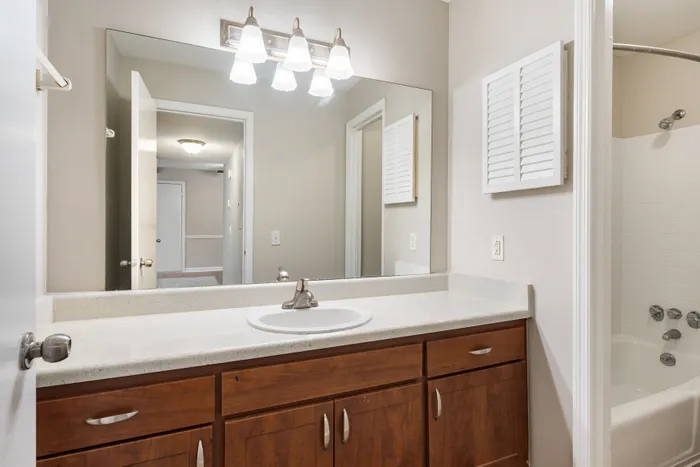 Modern bathroom with sleek white countertop, stylish lighting, and spacious wooden cabinetry, offering a serene and functional space.