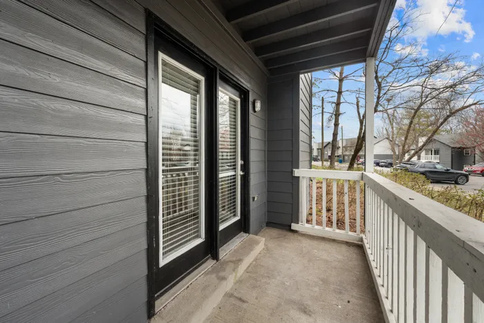 Charming apartment balcony with sleek gray siding, double doors with blinds, and a refreshing view of the outdoors.