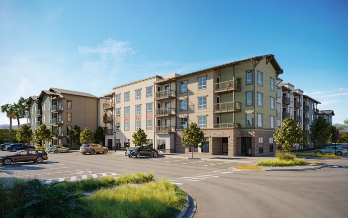 Modern apartment complex exterior with lush landscaping, ample parking, and inviting balconies under a clear blue sky.
