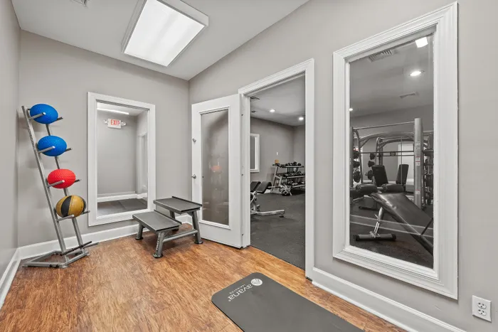 Modern gym space with equipment, exercise balls, and a weights area, featuring sleek wood floors and ample lighting.