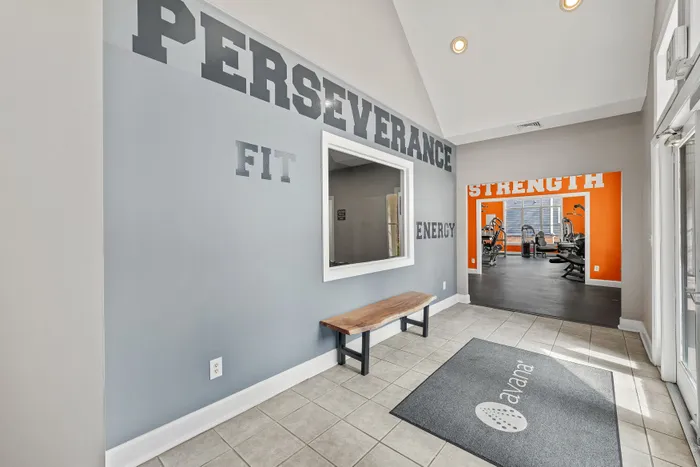 Inviting gym entrance with motivational words like 'Perseverance' and 'Strength', leading to a well-equipped fitness room.