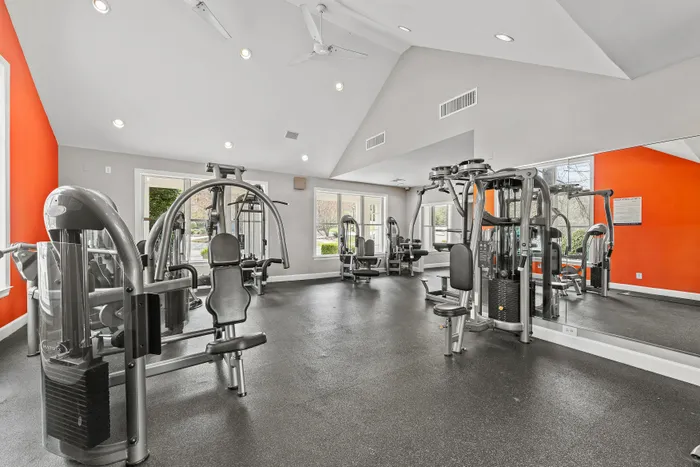 Contemporary fitness center with bright orange accents, featuring state-of-the-art exercise machines and ample natural light.