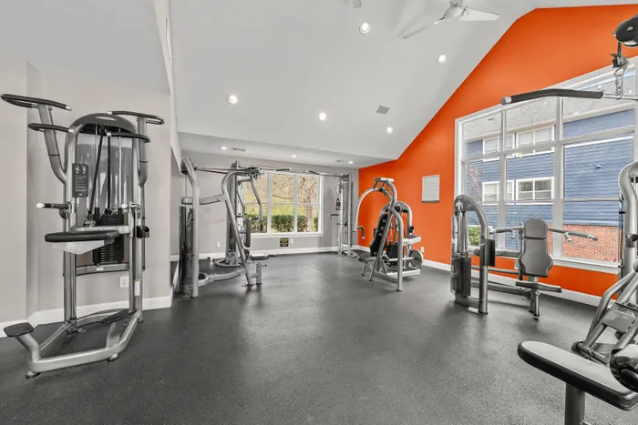 Modern gym with state-of-the-art fitness equipment and vibrant orange accent wall, offering a bright and inviting workout space.