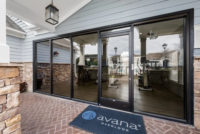 Inviting fitness center entrance with modern glass doors, showcasing exercise equipment and elegant stonework at Avana Overlook.
