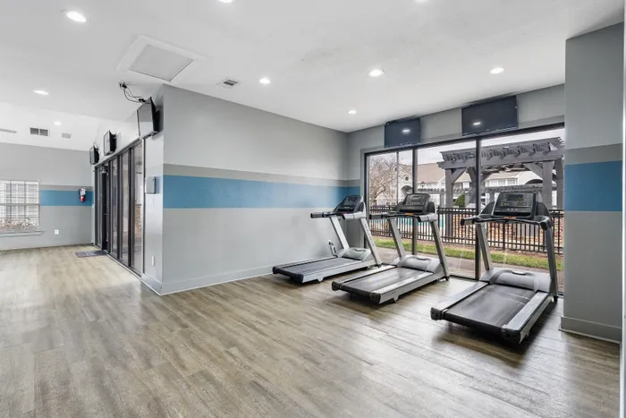 Modern fitness center with bright natural lighting, featuring three state-of-the-art treadmills facing a large window.