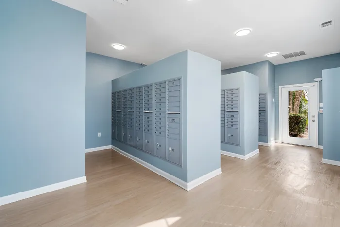 Modern apartment mailroom with sleek blue walls and well-organized mailboxes, featuring natural light through a glass door.