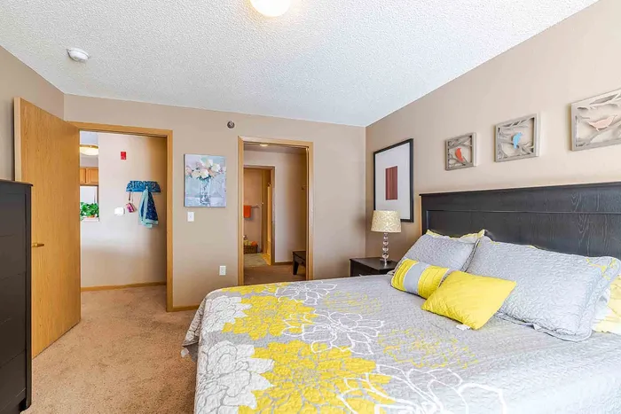 Bright and inviting bedroom featuring a cozy bed with elegant yellow and gray bedding, stylish artwork, and soft ambient lighting.
