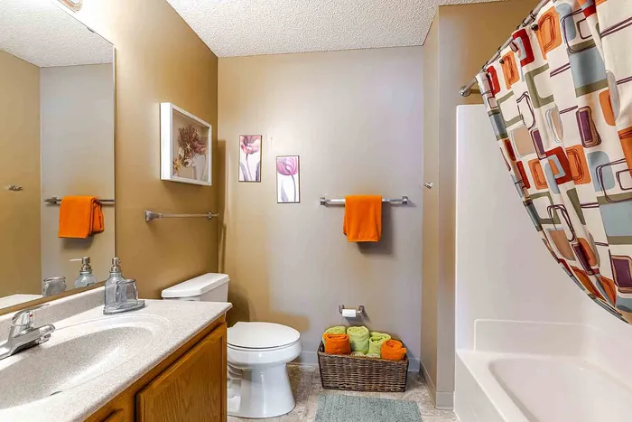 Elegant bathroom with modern fixtures, featuring stylish decor with orange and green accents, colorful shower curtain, and decorative wall art.
