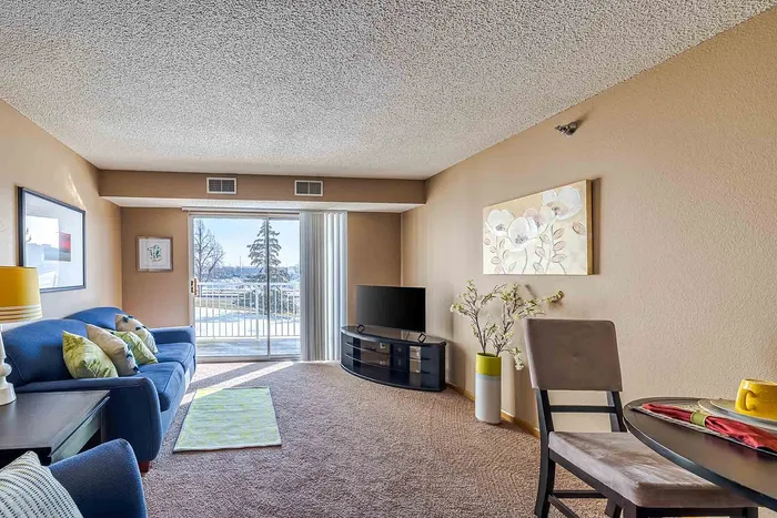Inviting living room with plush blue sofa, vibrant decor, and a sunlit balcony offering scenic outdoor views.