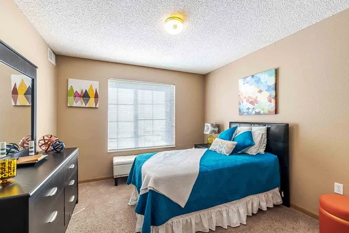Cozy bedroom with plush carpet, vibrant artwork, and a chic bed with bright blue bedding.