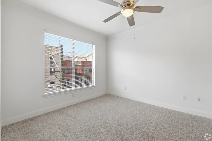 Bright airy bedroom with plush carpeting, large window, and modern ceiling fan, perfect for relaxation.