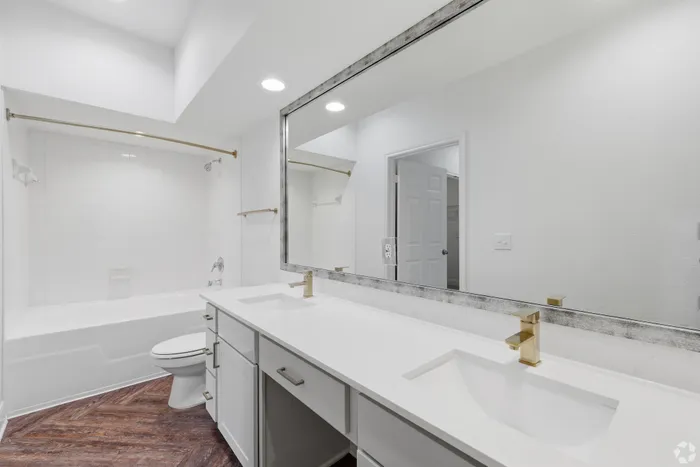 Elegant modern bathroom with double vanity, gold fixtures, and luxurious wood flooring.