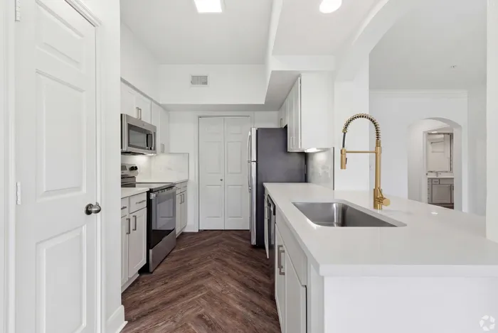 Contemporary kitchen with sleek white cabinetry, stainless steel appliances, and elegant wood flooring, featuring a chic gold faucet and ample counter space.