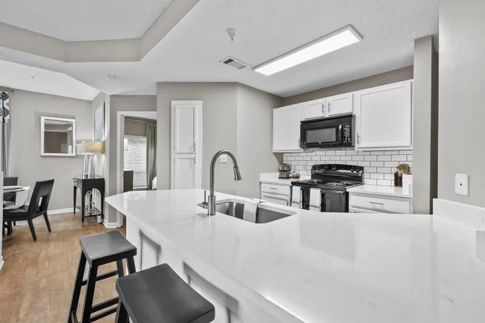 Modern kitchen with sleek white cabinets, a chic subway tile backsplash, and a spacious island with a built-in sink and breakfast bar seating, adjacent to a cozy dining area.