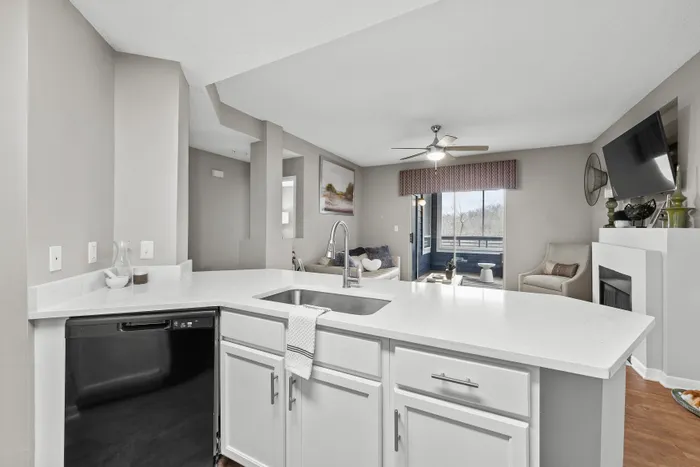 Bright and modern apartment kitchen with a sleek white island, open-concept layout, and cozy living area leading to a scenic balcony view.
