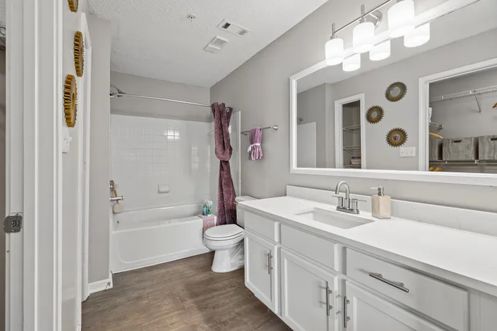 Modern and bright bathroom with elegant white cabinetry, sleek countertop, and stylish lighting, featuring a bathtub and chic wall decor for a luxurious touch.