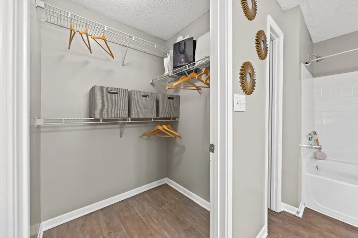 Chic and organized closet space with sleek shelving, elegant wooden hangers, and stylish storage bins adjacent to a modern bathroom.