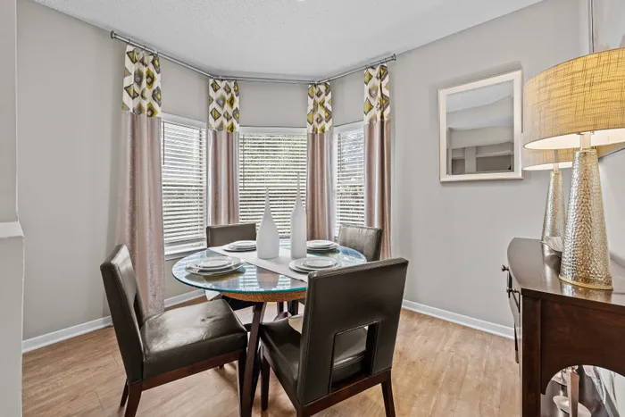 Elegant dining area with a round glass table, modern leather chairs, and chic decor in a bright, bay-window setting.