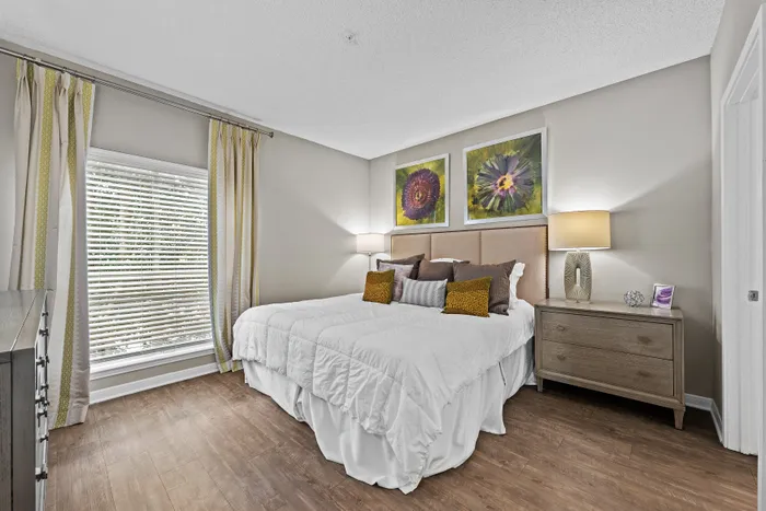Inviting bedroom featuring a plush king-size bed, elegant artwork, wooden flooring, and abundant natural light.