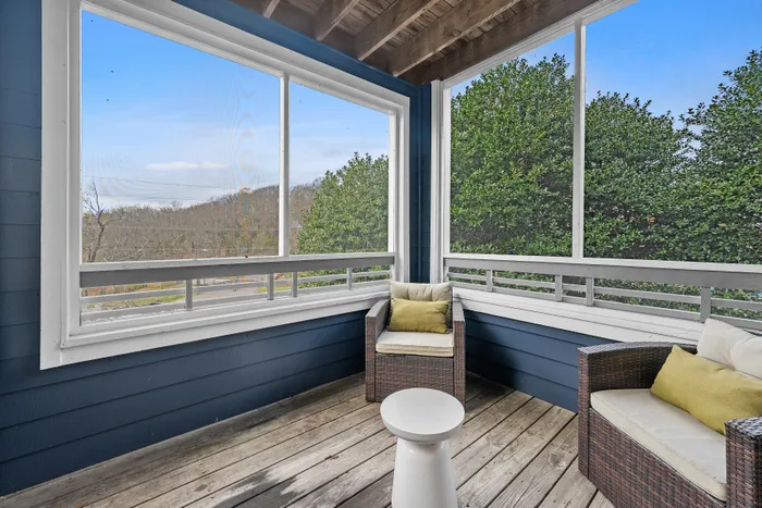 Charming screened porch with cozy rattan chairs and a scenic view of lush greenery, perfect for relaxation and enjoying nature.