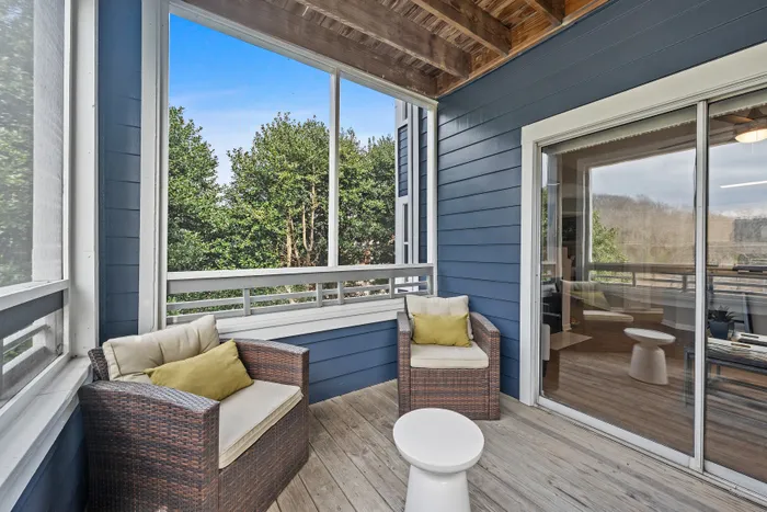 Charming covered balcony with cozy outdoor seating, surrounded by lush greenery, ideal for relaxation.