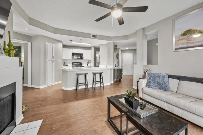 Modern open-concept living room with ceiling fan, cozy seating, and sleek kitchen bar in a stylish apartment.