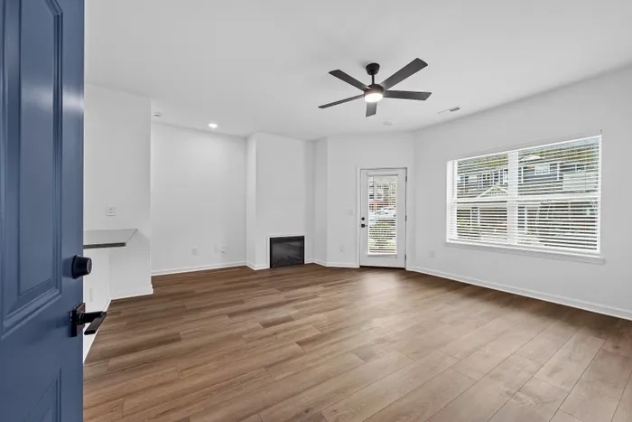 Bright and inviting living room with elegant wood flooring, modern ceiling fan, and expansive windows overlooking serene views.