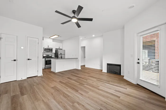 Modern apartment living area with sleek hardwood floors, open-plan kitchen featuring stainless steel appliances, and a cozy fireplace.