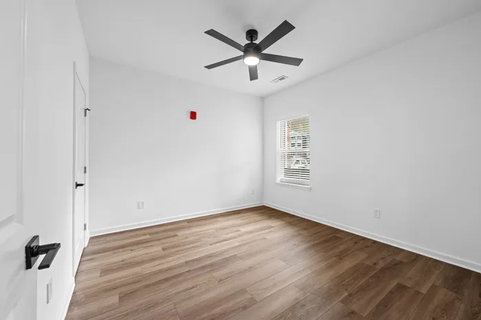 Bright and airy bedroom featuring elegant wood flooring, a sleek modern ceiling fan, and a sunlit window with blinds.