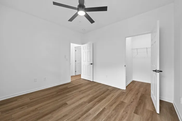 Bright and modern bedroom with sleek wooden flooring, ceiling fan, and spacious closet access.