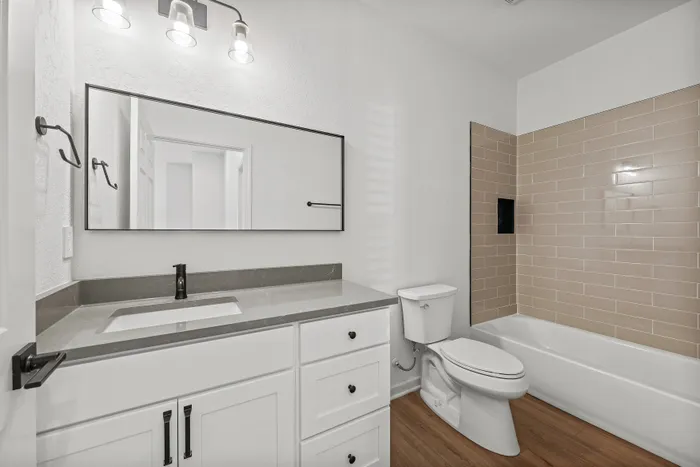Modern bathroom with sleek white cabinetry, elegant wall-mounted lighting, and a stylish bathtub with neutral tile accents.