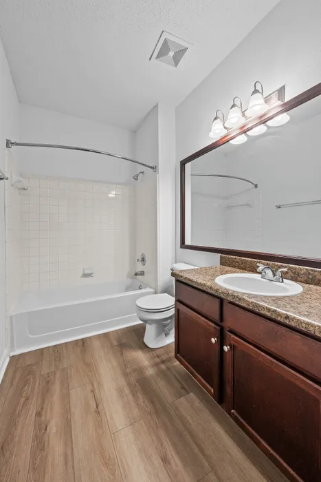 Contemporary bathroom with elegant wood flooring, a stylish granite countertop, and a pristine bathtub area.
