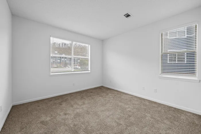 Bright, spacious room with plush carpet and large windows, offering an inviting and serene vibe.