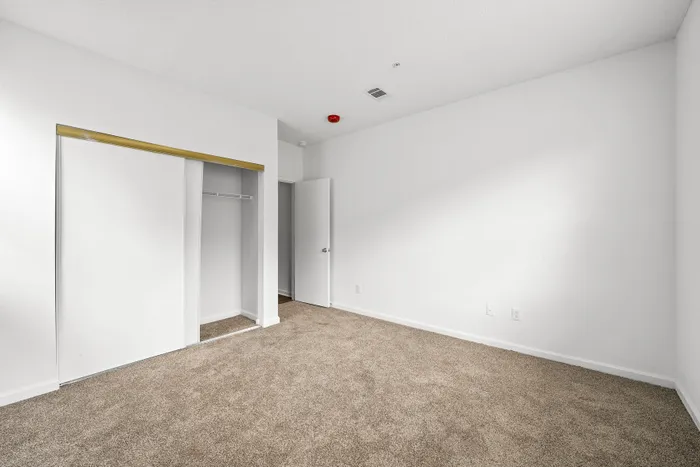 Bright and spacious empty room with soft carpet and sliding closet doors, perfect for customization and creating a cozy living space.