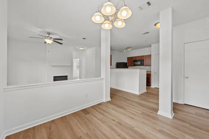 Elegant open living space featuring a ceiling fan, modern chandelier, and sleek hardwood floors, leading into a cozy kitchen with wooden cabinetry.