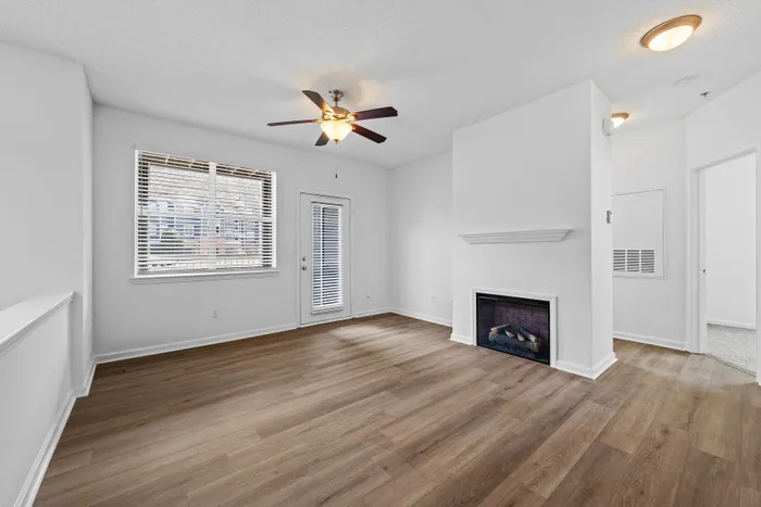 Bright living room with elegant hardwood flooring, a modern ceiling fan, and a cozy fireplace, perfect for relaxation and entertainment.