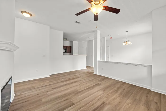 Bright open floor plan with elegant wood flooring, modern lighting, and a cozy kitchen in an inviting apartment setting.