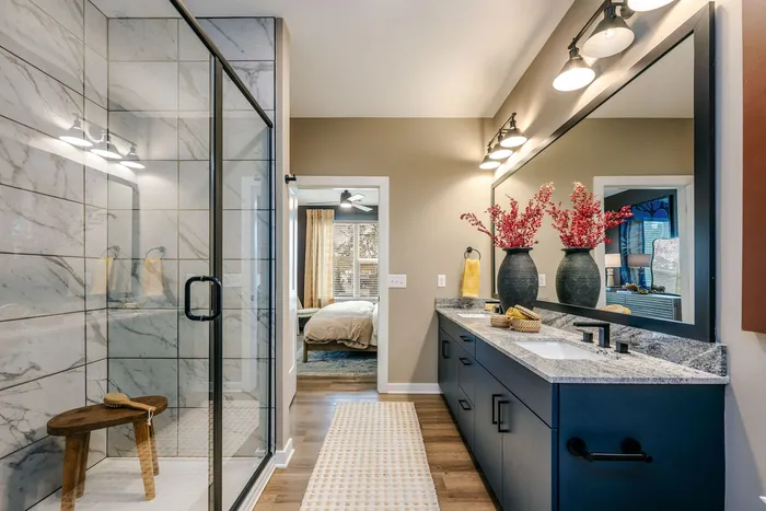 Elegant bathroom featuring a luxurious marble shower, modern vanity with double sinks, and stylish decor leading to a cozy bedroom.