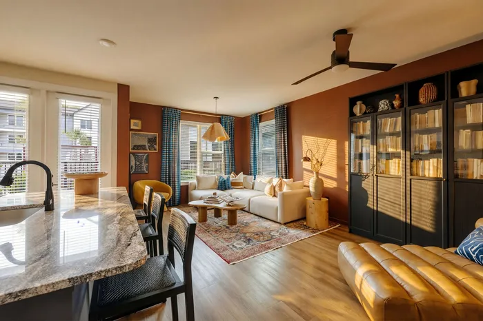Inviting living space featuring a cozy sectional, elegant wooden flooring, natural light from large windows, and a stylish breakfast bar.