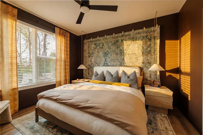 Cozy bedroom with warm tones, featuring a stylish bed, elegant wall tapestry, and large windows with soft natural light.
