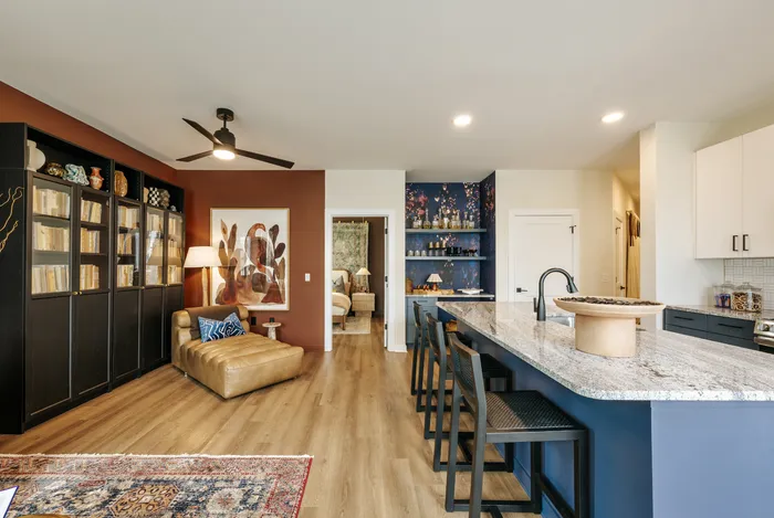 Modern open-concept living area featuring a cozy seating nook, stylish bookshelves, and a spacious granite kitchen island, perfect for entertaining.