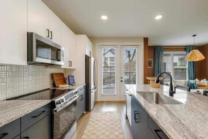 Modern kitchen with sleek granite countertops, stainless steel appliances, and bright natural light from large patio doors.