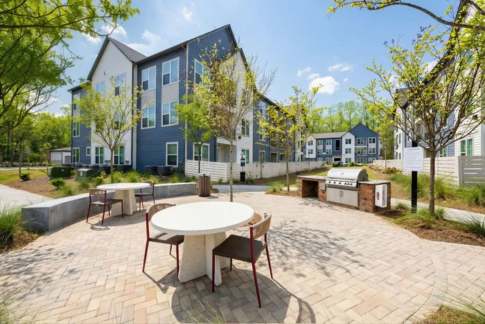 Sunny apartment courtyard with modern outdoor seating, lush landscaping, and a built-in grill area for community gatherings.