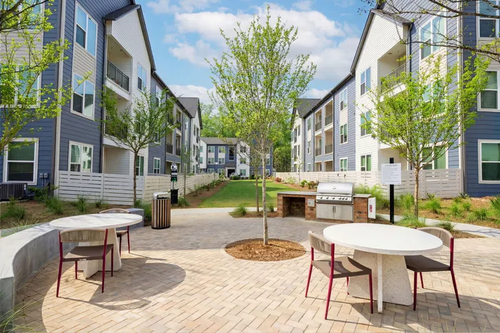 Charming apartment courtyard showcasing modern outdoor dining area, barbecue station, and lush greenery for a perfect communal gathering space.