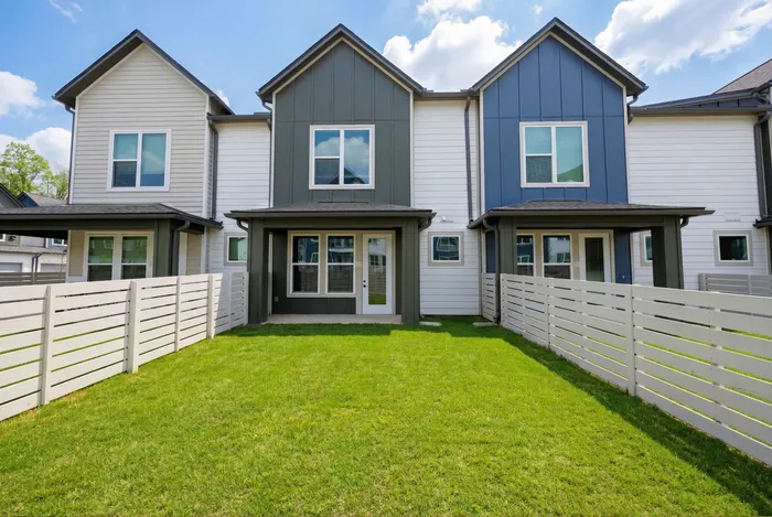 Charming townhouse with modern facade, spacious fenced backyard, and inviting green lawn under a clear sky.