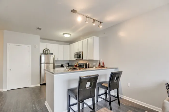 Modern kitchen with sleek stainless steel appliances, elegant white cabinetry, and a cozy breakfast bar featuring stylish leather stools.