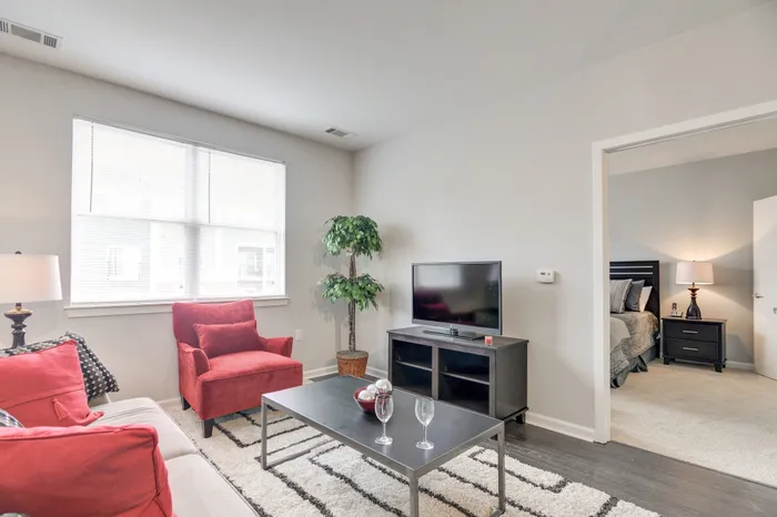 Bright, modern living room with chic red accents, natural light, and cozy bedroom view.