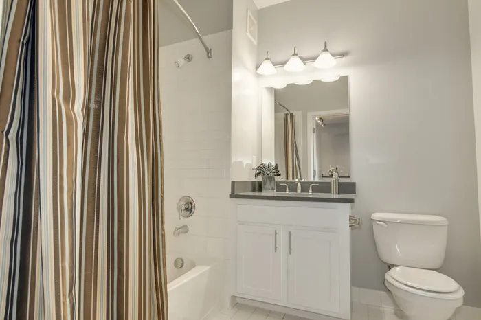 Elegant bathroom featuring a chic vanity, striped shower curtain, and bright lighting in a serene setting.